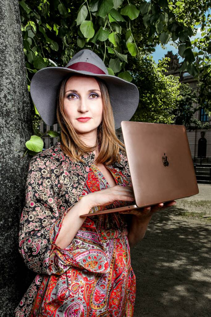 Frau steht und hält einen Macbook in der Hand