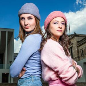 Two women stand back to back and look into the camera